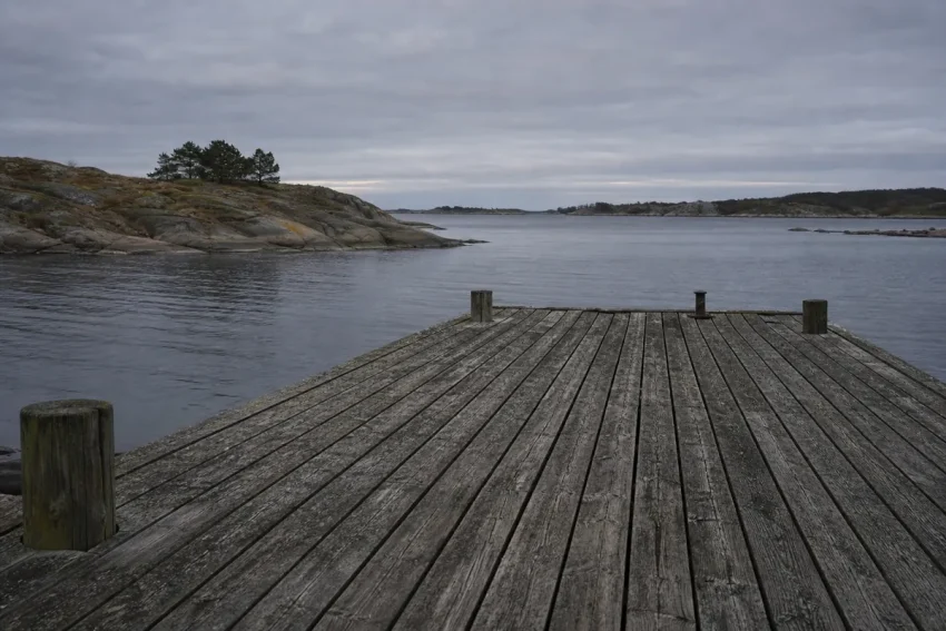 Sliten trbrygga i skärgården i gryningsljus med låga klippöar i bakgrunden